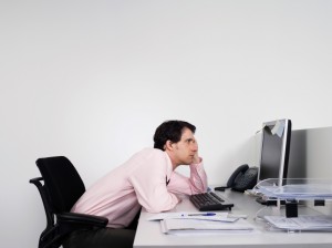 Side view of a bored male office worker looking at notes on computer monitor at desk